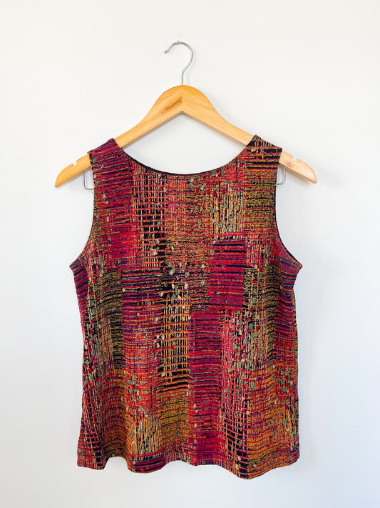 A vintage sleeveless top with a multicolored geometric pattern, hanging on a wooden hanger against a white background.